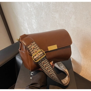 Detailed view of brown leather bag with golden buckle and geometric woven wide strap