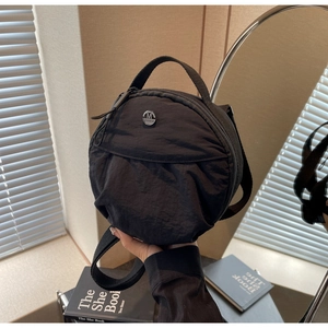 Gros plan d'un sac bandoulière rond en nylon noir avec une plaque logo M FASHION en métal