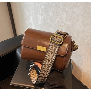 Detail of a brown leather crossbody bag with a vintage patterned wide woven strap