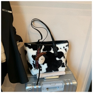 Detail of fuzzy cow print tote bag with cute cartoon charm and black shoulder strap
