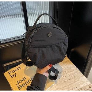 Gros plan d'un sac rond en nylon noir avec logo M métallique et fermeture éclair double