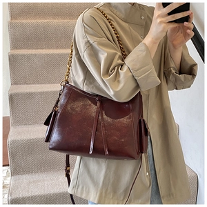 Dettaglio della borsa tote in pelle lucida bordeaux con catena metallica e tasca laterale