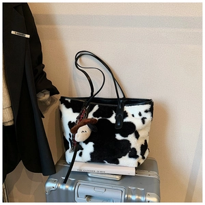 Close-up of cow print plush tote bag featuring soft faux fur and cute puppy charm detail