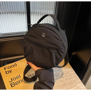 Détail du sac à bandoulière rond en nylon noir avec logo argenté sur marbre