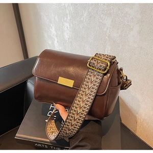 Detail of vintage brown pillow bag with textured geometric jacquard wide strap on books