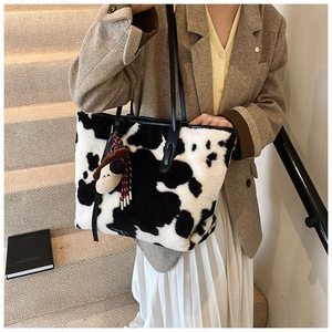 Detail of cow print plush tote bag with furry animal pendant and sleek black straps