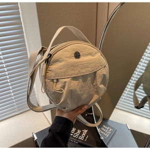Détail du petit sac rond en nylon beige avec bandoulière réglable et logo en métal