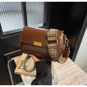 Close-up of vintage brown crossbody bag with retro patterned wide strap and gold buckle