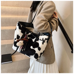 Close-up of a large cow print plush tote bag with a cute puppy pendant on shoulder