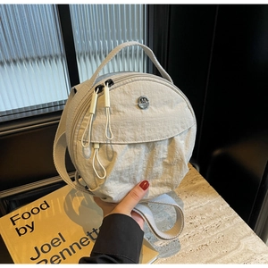 Détail du sac rond gris en nylon avec logo M en métal sur surface en marbre