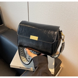 Detail of glossy black pillow bag with gold metal buckle and woven wide strap