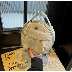 Détail d'un sac bandoulière rond en nylon beige avec logo argenté et double zip