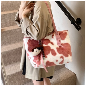 Detail of pink cow print plush tote bag with a matching fuzzy cow charm on a leather strap