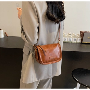 Détail d'un sac bandoulière en cuir marron avec texture vintage et plaque logo en métal