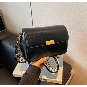 Detail of black faux leather bag with gold buckle and black-white woven wide strap