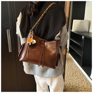 Dettaglio della borsa tote marrone scuro in pelle lucida con catena dorata e nappe decorative