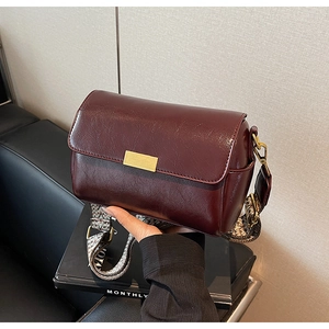 Detail of burgundy leather handbag featuring wide jacquard woven strap and gold buckle