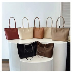 Collection of large leather tote bags in seven colors displayed on white pedestals