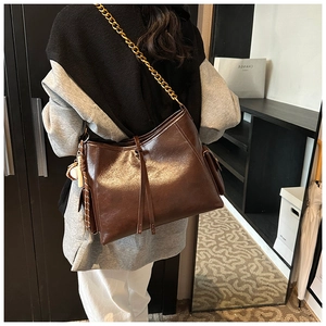 Dettaglio borsa a spalla in pelle lucida marrone scuro con catena dorata e nappa decorativa