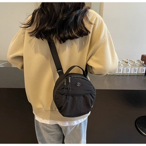 Détail du sac à bandoulière rond en nylon noir montrant la texture et la poche avant