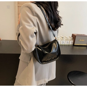 Détail d'un sac demi-lune en cuir noir sur un mannequin portant un blazer gris