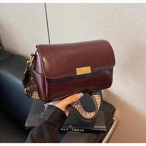 Detail of burgundy leather pillow bag with colorful geometric woven wide strap and gold hardware
