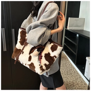 Close-up of fluffy cow print plush tote bag featuring a cute cartoon dog charm and leather straps