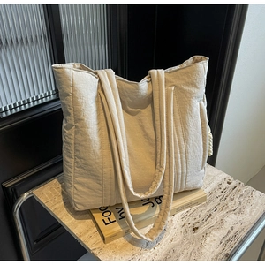 Detail view of the quilted texture and wide shoulder straps on this beige tote bag