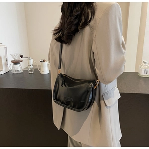 Détail d'un sac bandoulière en cuir noir avec logo métallique et fermeture éclair élégante