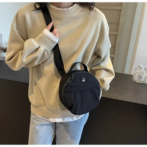 Détail d'un petit sac rond noir en nylon avec bandoulière réglable porté par un mannequin