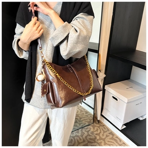 Dettaglio borsa tote in pelle lucida marrone scuro con catena dorata e charm baseball