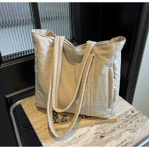 Detail of beige tote bag with natural pleated texture and side zipper on a marble surface