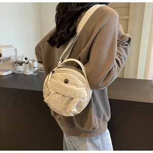 Vue détaillée d'un sac bandoulière rond en nylon beige porté par un mannequin dans un café