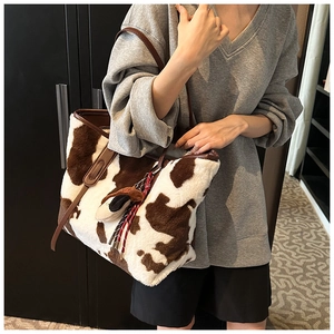 Detail of soft faux fur cow print tote bag with brown leather handles and charm