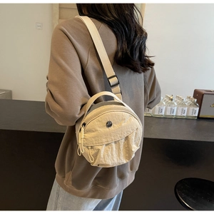 Vue détaillée d'un sac rond en nylon beige avec logo en métal et bandoulière réglable