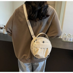 Détail d'un sac rond en nylon beige montrant la texture plissée et le logo métallique