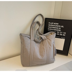 Macro shot of light gray quilted nylon tote bag with textured surface and woven pendant