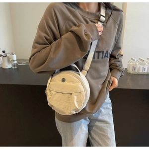 Détail du sac rond en nylon crème avec texture plissée et bandoulière réglable