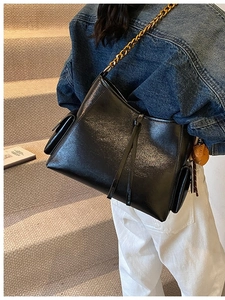 Borsa a spalla nera lucida con catena dorata e ciondolo a orsetto in scena urbana
