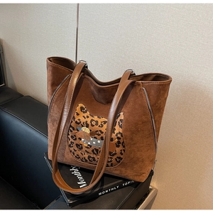 Detail of a brown suede tote bag with leopard cat embroidery on a leather sofa