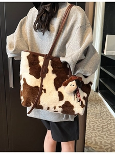 Large cow print plush tote bag with brown straps and cute charm worn by a model