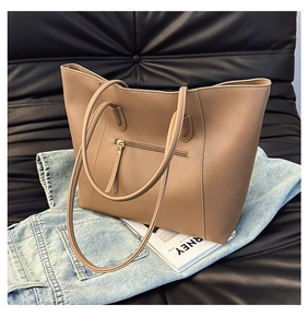 Detail view of khaki leather tote bag with front zipper pocket on a dark sofa
