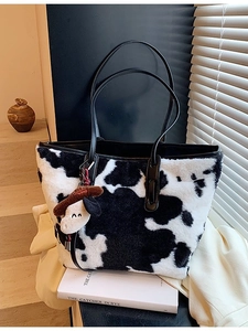 Fuzzy cow print tote bag with plush material and black leather straps in home setting