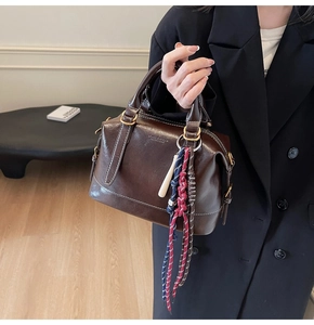 Dettaglio della borsa Boston vintage marrone scuro con cuciture bianche e ciondolo in corda