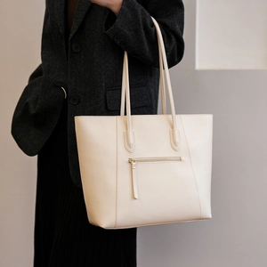 Detail of cream tote bag with rear zipper pocket and long leather handles on model