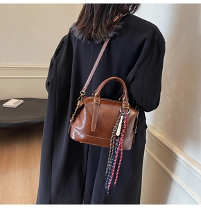 Dettaglio borsa Boston in pelle marrone con cuciture a contrasto e ciondolo intrecciato