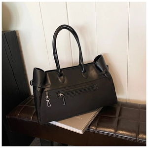 Detail of a black large tote bag featuring leather-canvas texture and metal carabiner charm