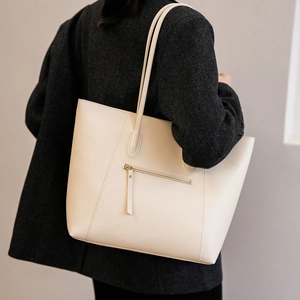 Detail of a creamy white leather tote bag with a zipper pocket on a model's shoulder