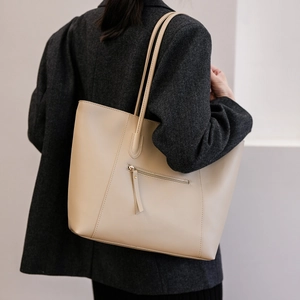 Detail of a large beige leather tote bag with side zipper and dual slim shoulder straps