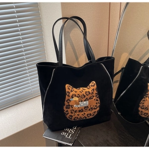 Detail of black suede tote bag featuring a leopard patch and silver zipper accents